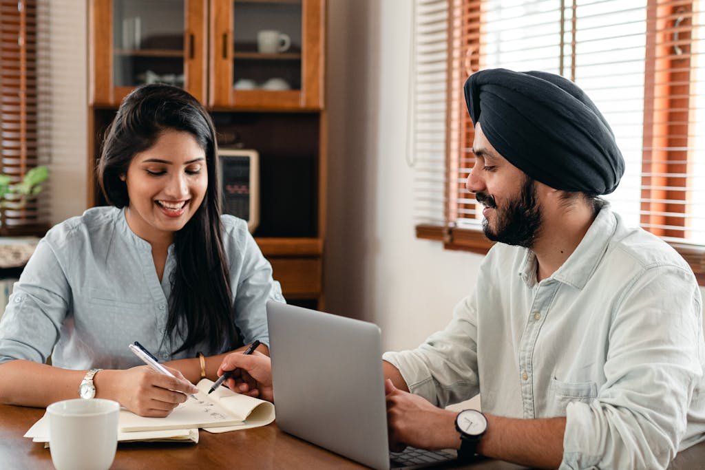 Smiling couple working on a project with a laptop at home, showcasing teamwork and connection.